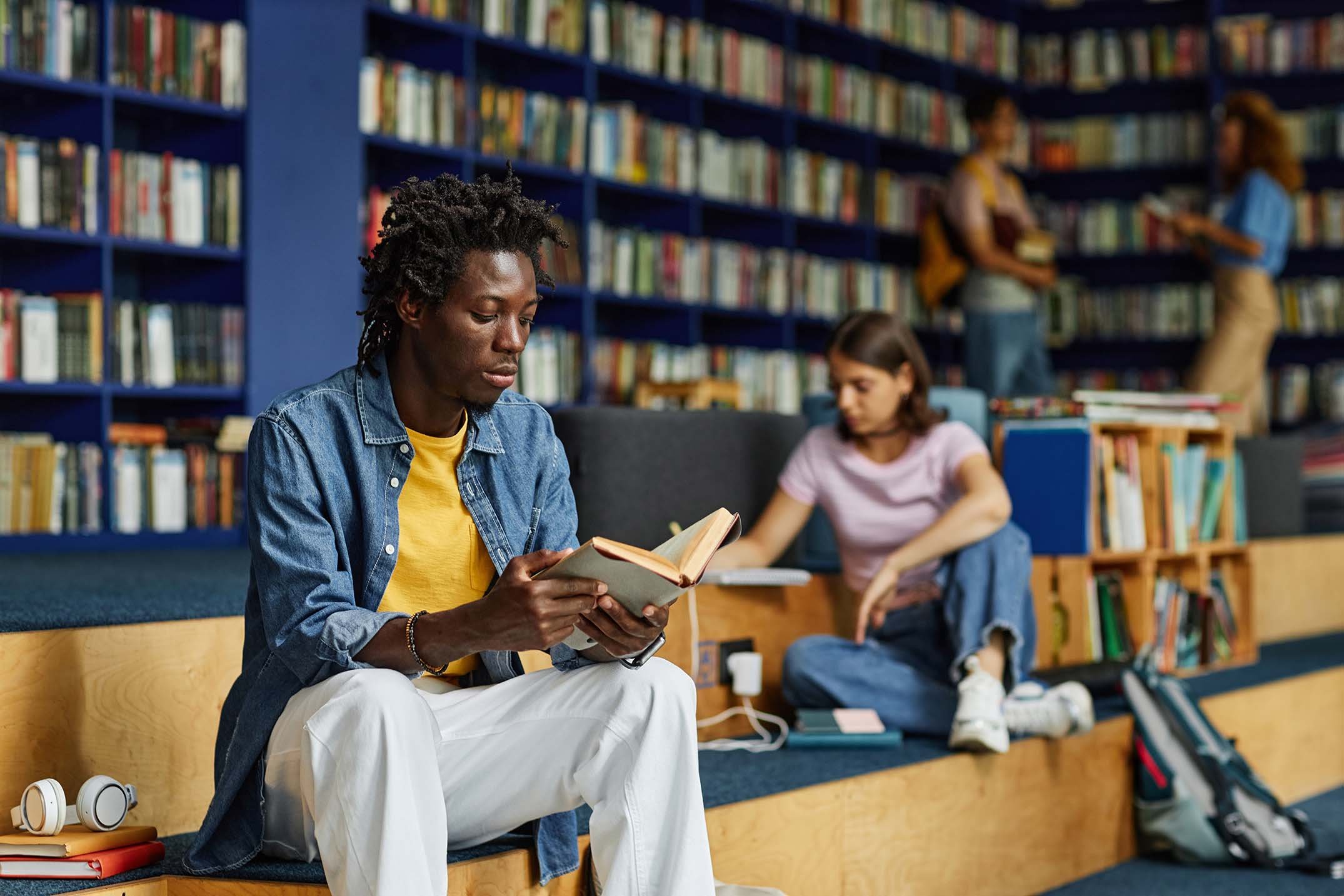 Young black man reading a book in a library.