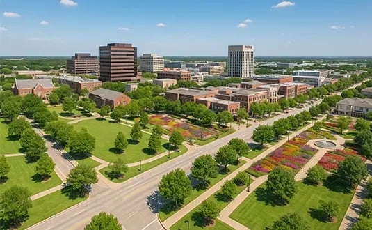 Aerial view of Plano, Texas showing clean streets, landscaped parks, tree-lined roads, and modern buildings under a bright blue sky.