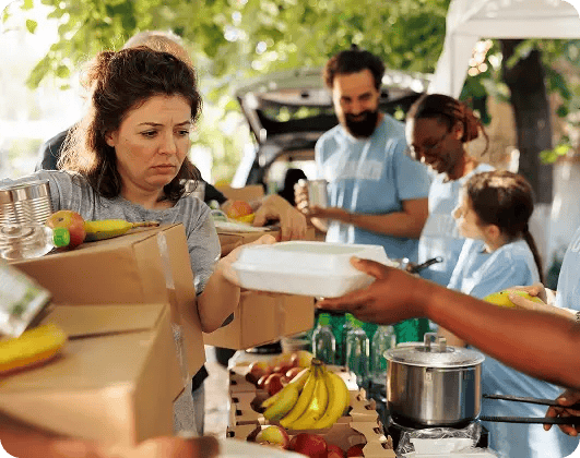 Volunteers serving hot meals and distributing food boxes with fresh fruit at a community food bank event.