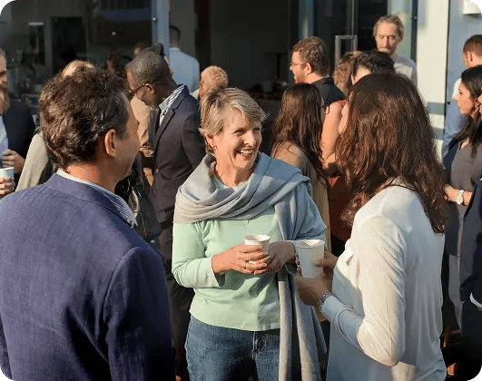 Group of people smiling and talking at an outdoor gathering, symbolizing community connection and support in hospice care.