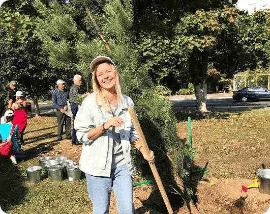 Smiling young woman planting a tree during a community volunteer event in a park.