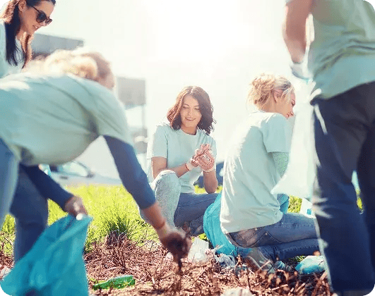 Volunteers in light blue shirts picking up trash and cleaning a grassy park area.