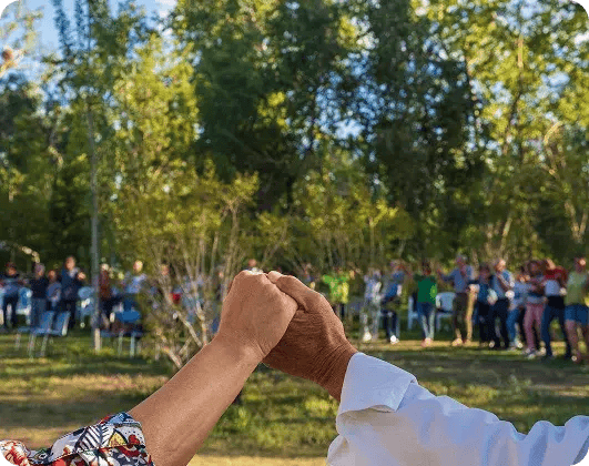 Close up of two people holding hands outdoors during a community gathering in a park.