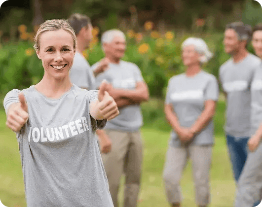 Smiling volunteer giving two thumbs up with her team standing in the background.
