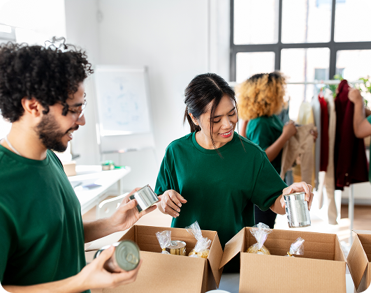 Volunteers smiling while packing canned food and dry goods into donation boxes.