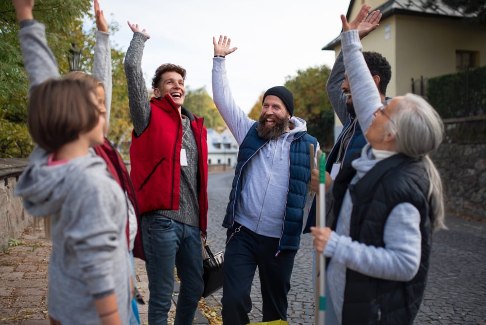 Group of enthusiastic volunteers outdoors celebrating with raised hands, symbolizing teamwork, community impact, and the spirit of volunteerism.