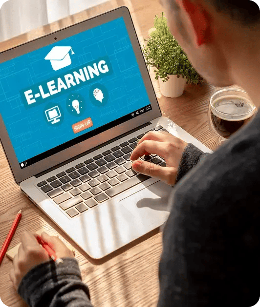 Person using a laptop displaying an e-learning screen, with a notebook and drink nearby.