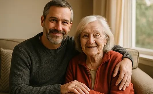 Middle-aged volunteer and elderly woman sitting together in a cozy living room, smiling warmly to reflect dignity, care, and companionship.