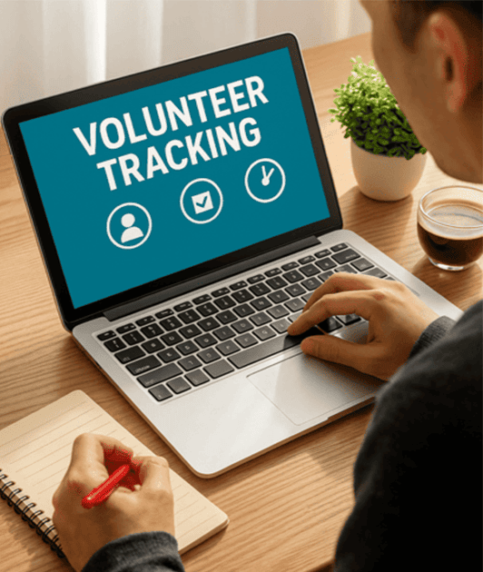 Person working on a laptop with the screen displaying 'Volunteer Tracking', taking notes with a red pen.